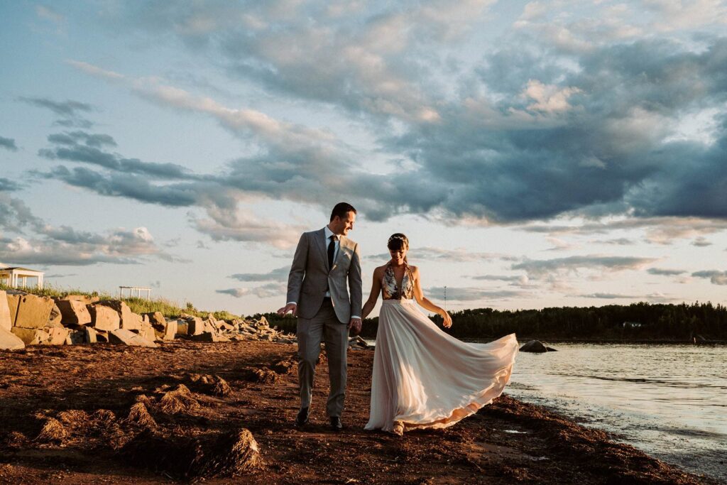 A couple hand in hand by water with a dynamic sky