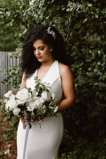 Bride in a white dress holding and looking at her white bouquet of flowers