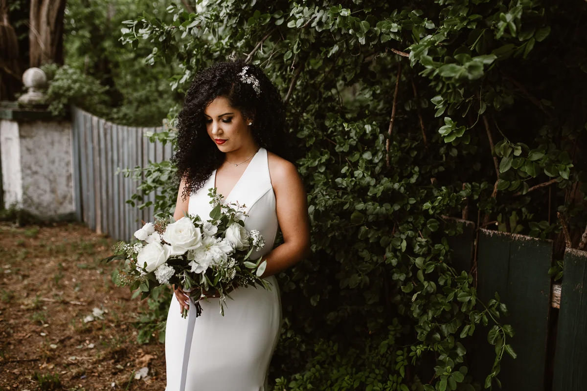 Bride in a white dress holding and looking at her white bouquet of flowers