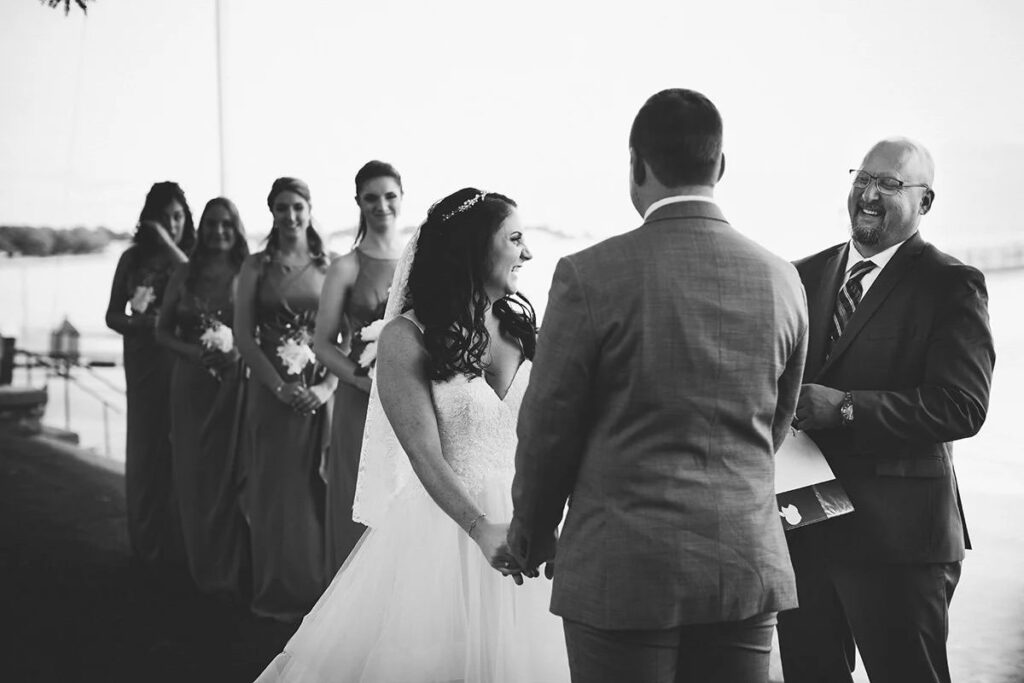 A black and white image of a bride and groom at their ceremony with all their bridesmaids behind