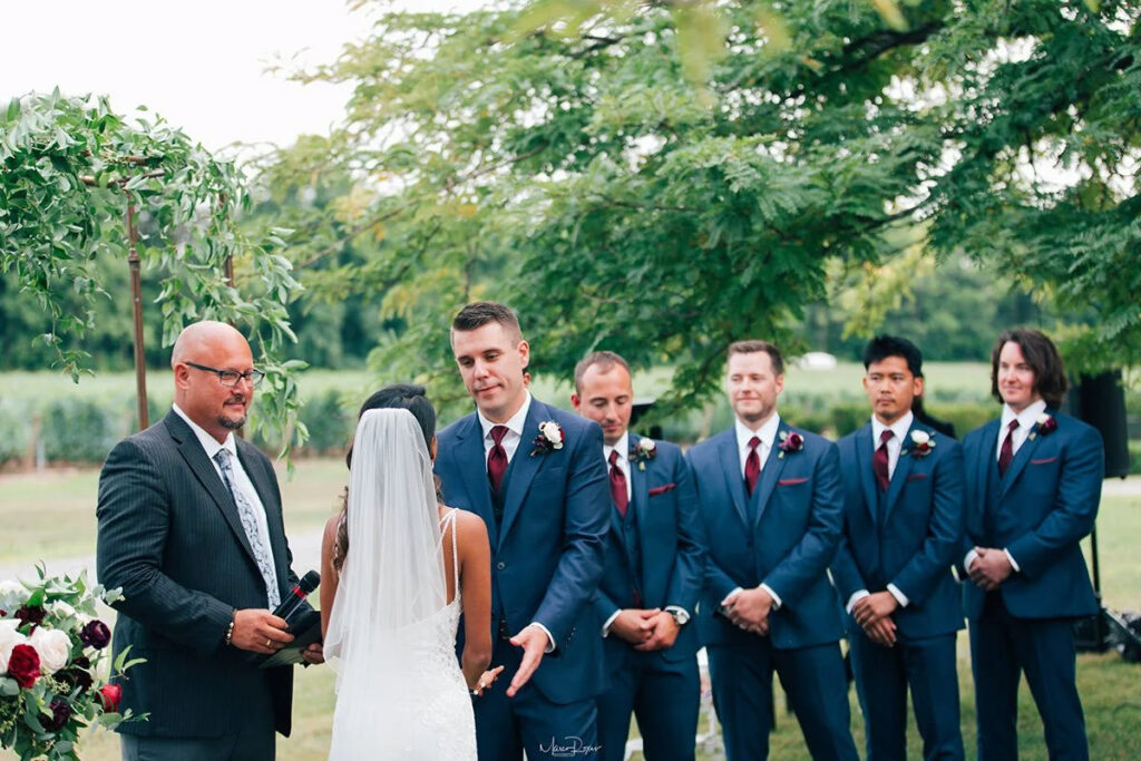 A bride and groom at their ceremony with a all their groomsmen behind the groom