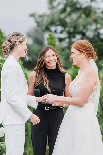 Two brides at their ceremony with lots of white florals behind