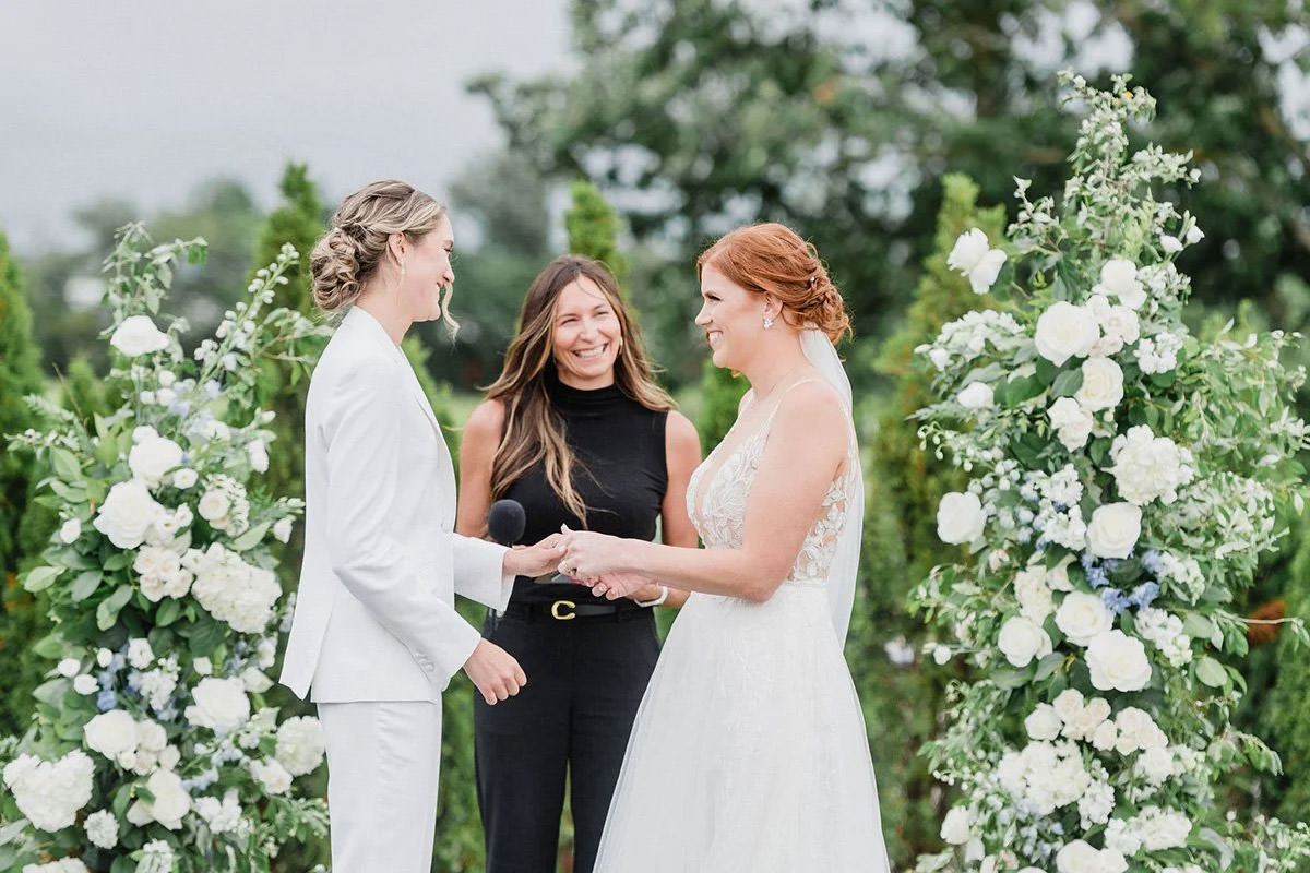 Two brides at their ceremony with lots of white florals behind