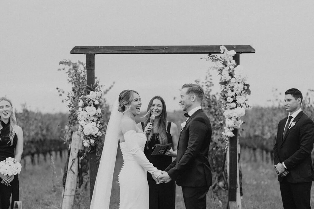 A black and white image of a bride and groom at their ceremony laughing