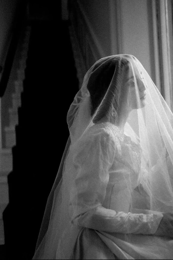 A bride with her veil over her head gazing out a window
