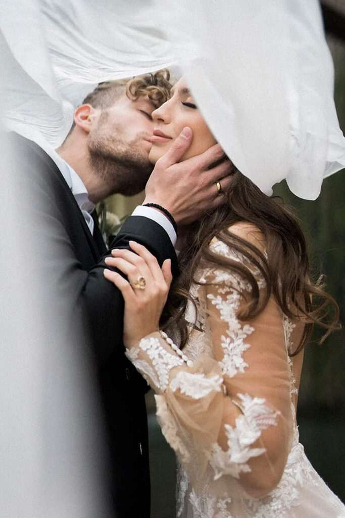 From under a wedding veil, a couple embracing