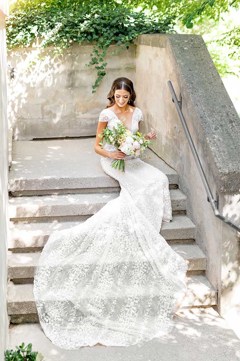 A bride sitting on concrete stairs with her dress cascading down