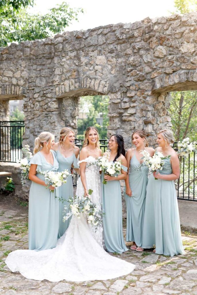 Bride and her bridesmaids together holding their flowers and laughing