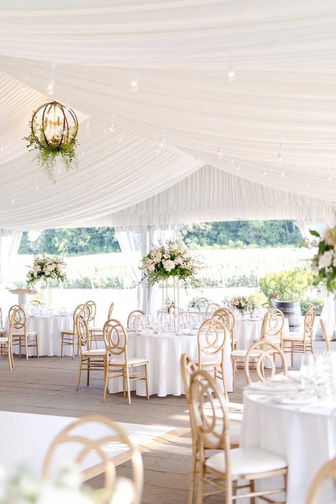 A tented venue with white draped ceiling, and gold chairs