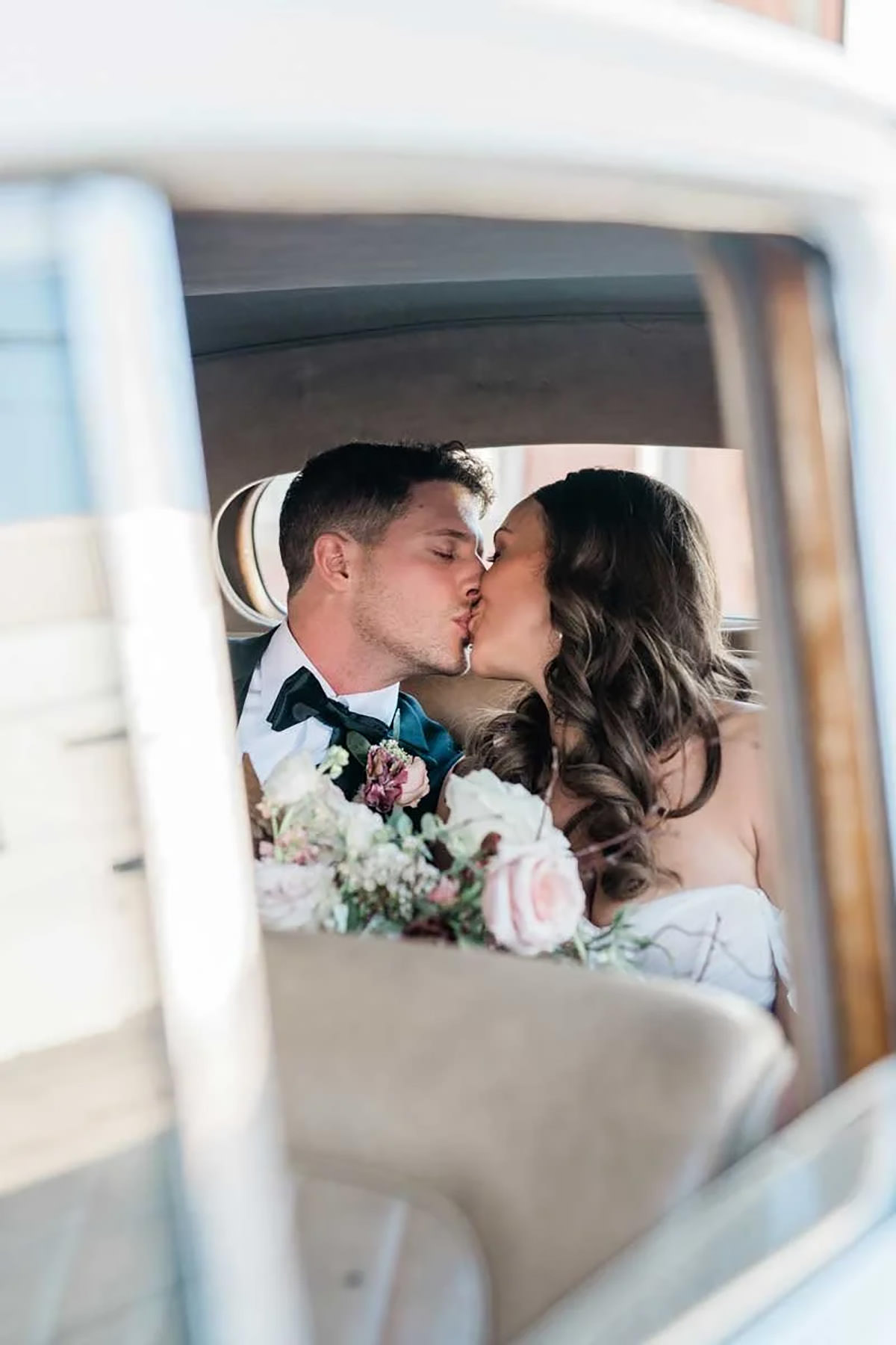 A photo through a car window of a bride and groom kissing