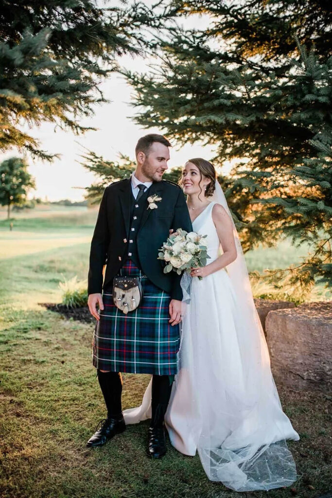 A bride hanging onto the arm of her groom in his tartan