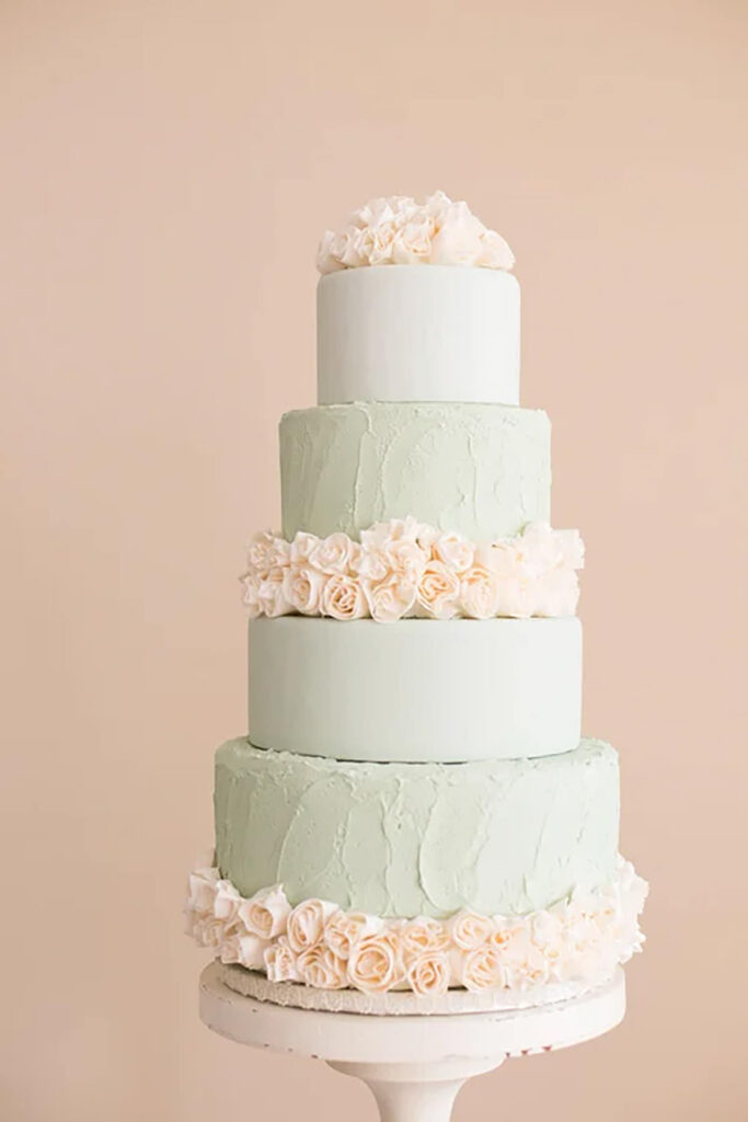 A 5 tier pale green cake with light flowers on it
