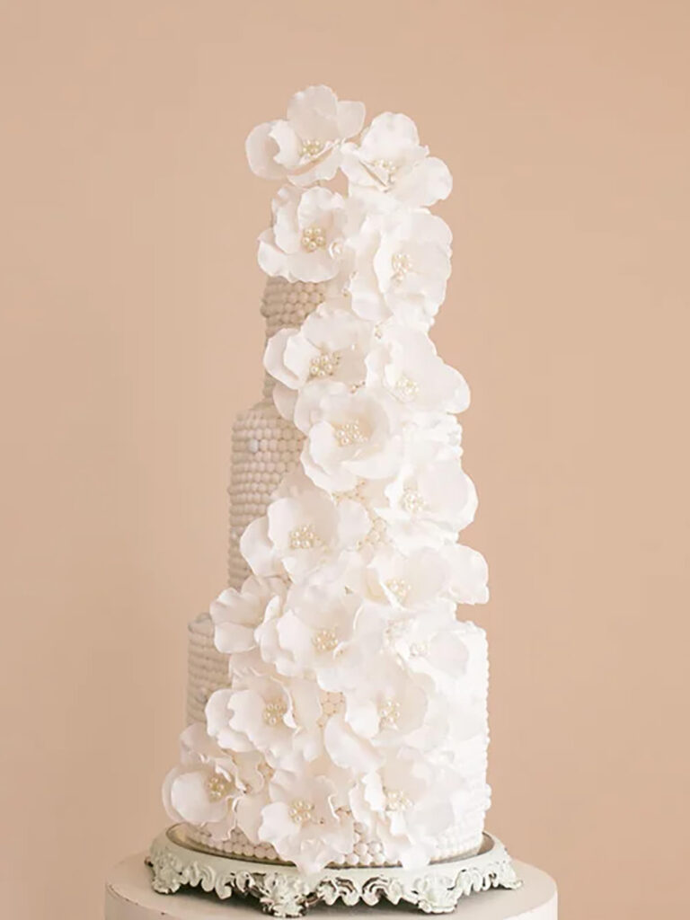 A 3 tier white cake covered with pearls and flowers on it