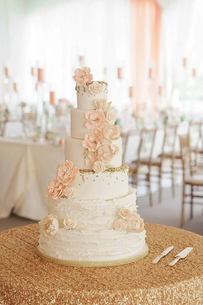 A 6 tier with flowers on it, on a golden sequined tablecloth