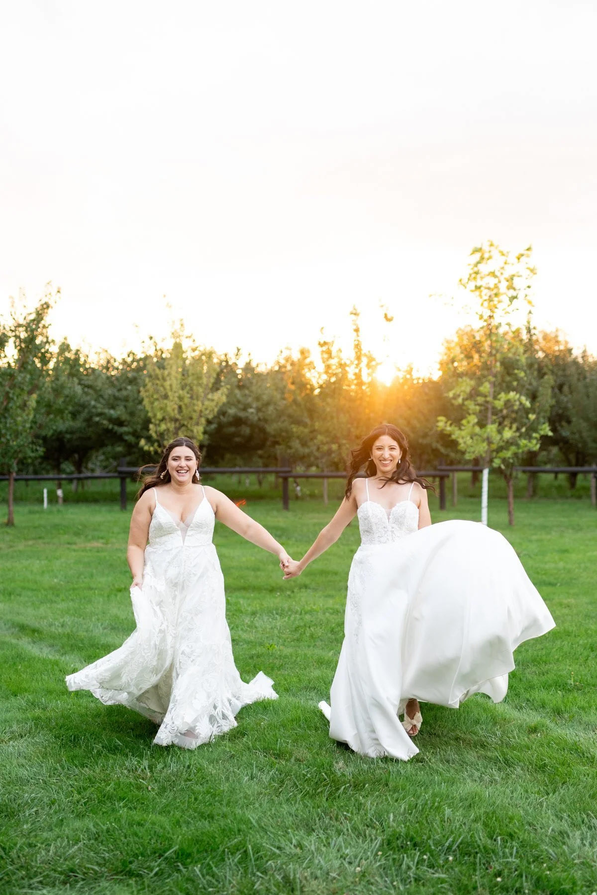 Two brides running through a a grassy area holding hands