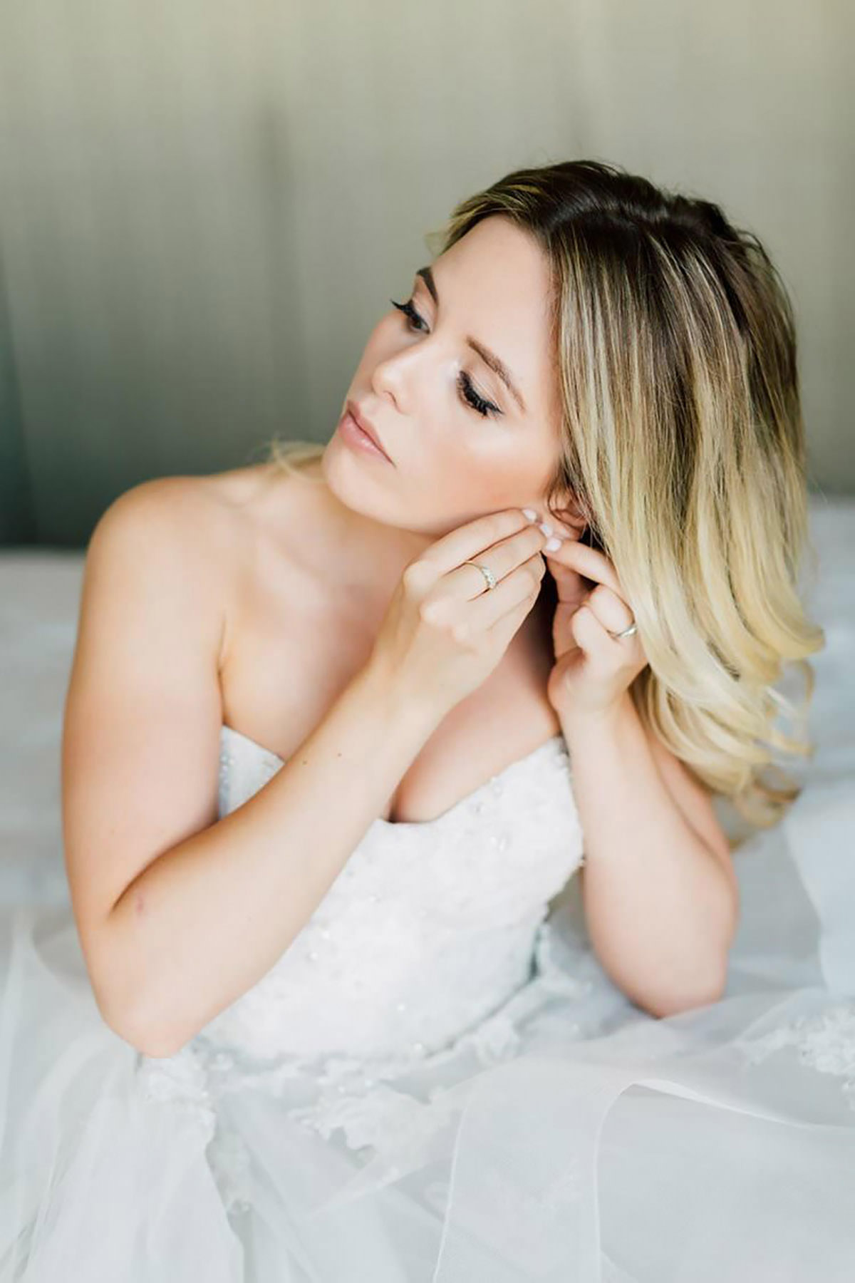 A bride putting her earrings in sitting on a bed