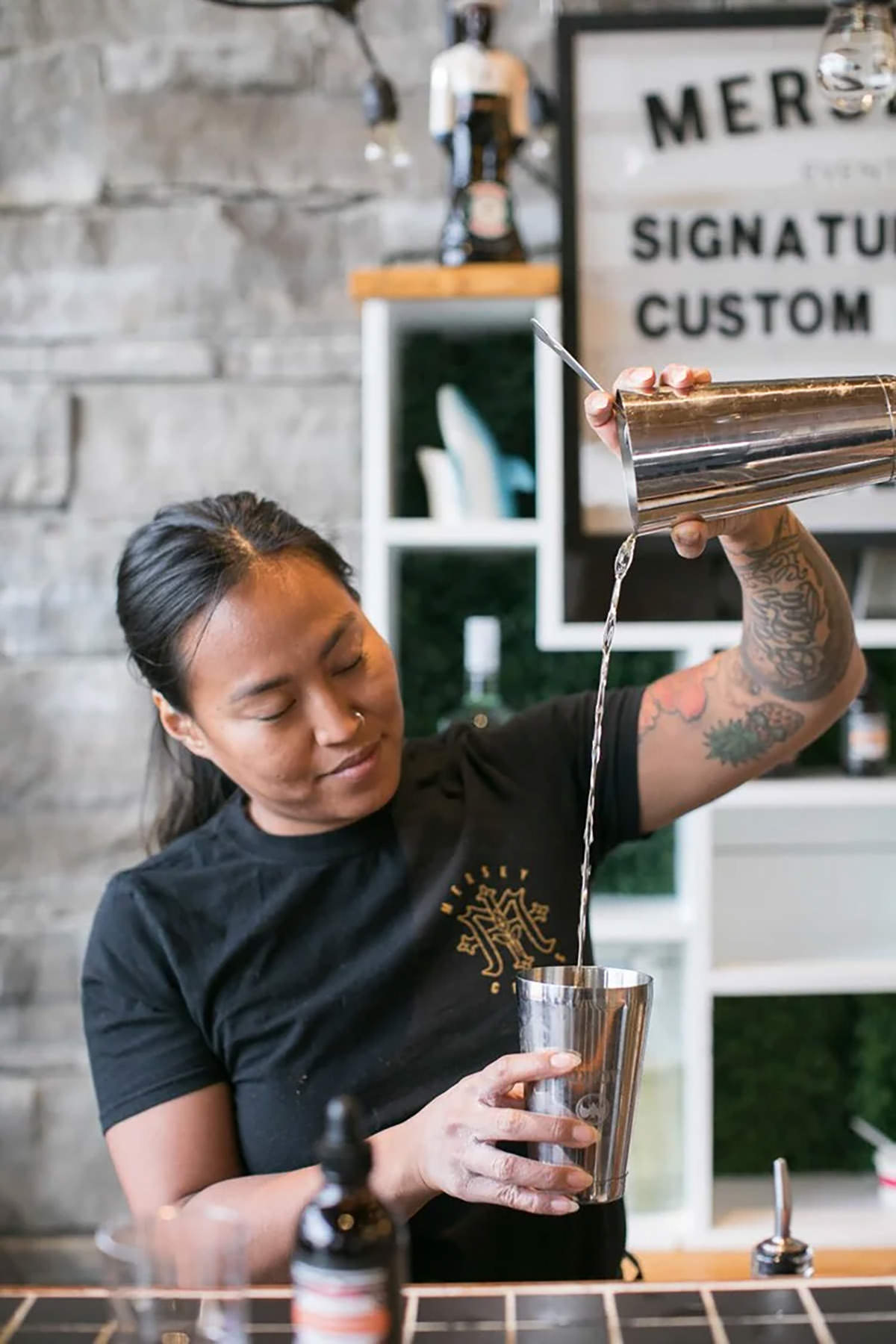 A bartender mixing a drink and pouring from high
