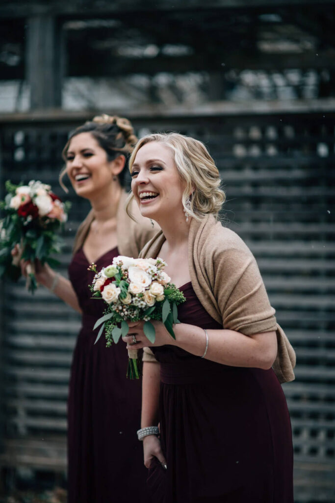 A couple of bridesmaids laughing wearing maroon dresses and shawls