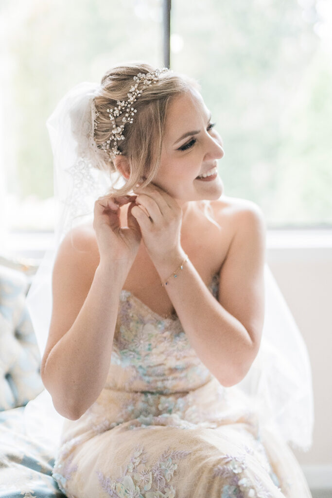 A bride smiling while putting on earrings.