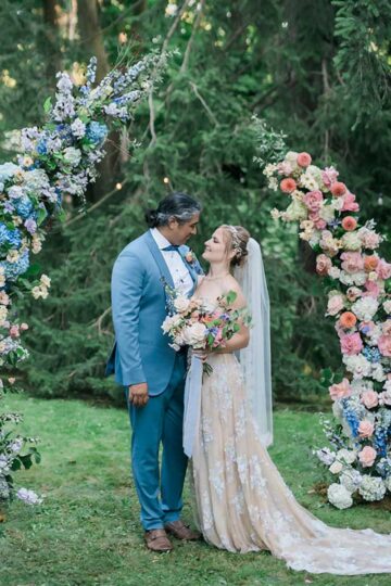 A couple standing under an arch of colourful flowers.
