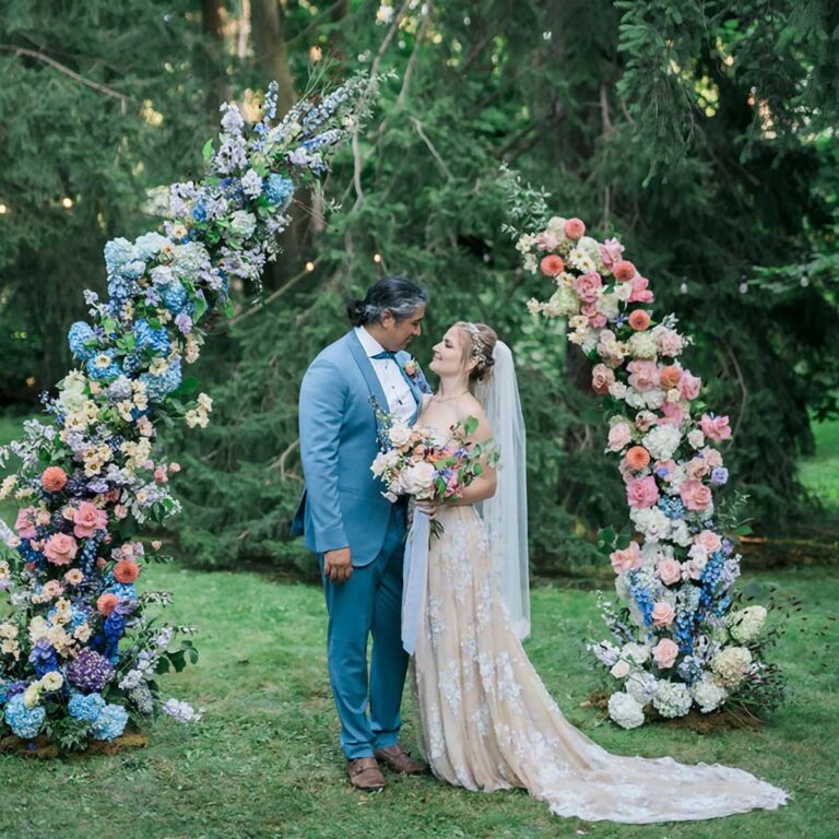 A couple standing under an arch of colourful flowers.