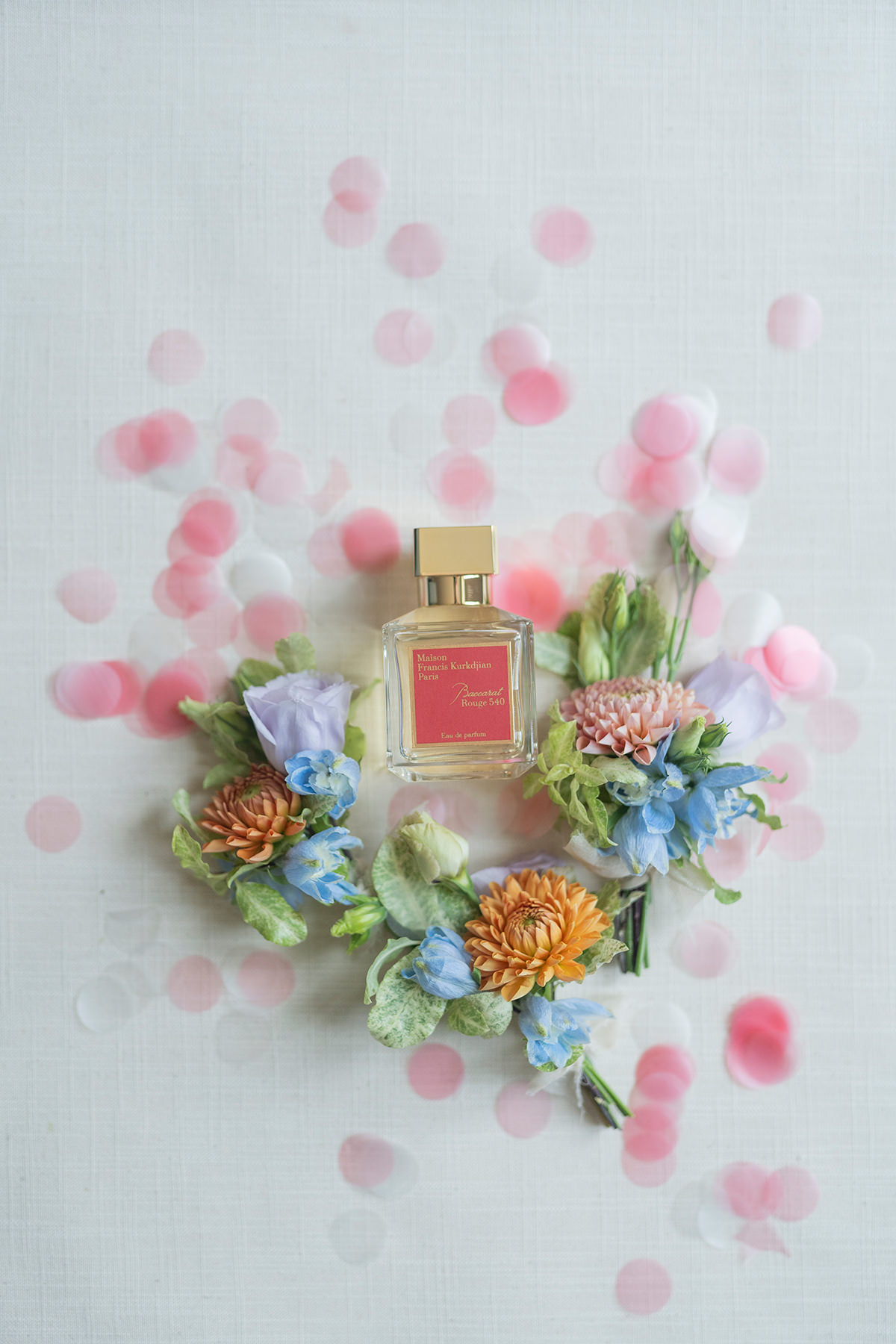 flatlay of bridal perfume and boutonnières on pink confetti
