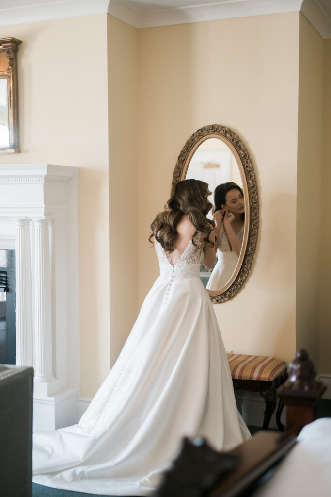bride putting earrings on in an oval mirror