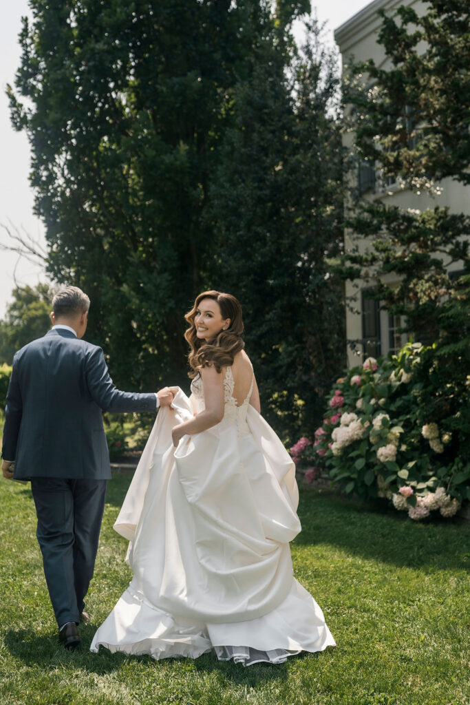 groom carrying the train of his bride's dress while she looks back