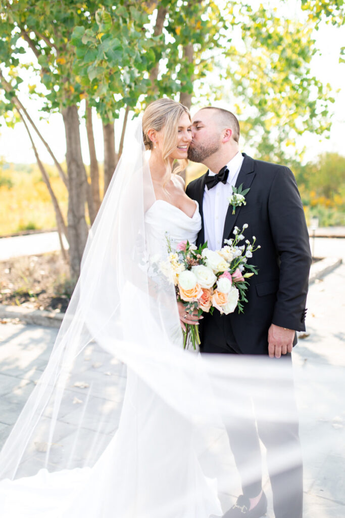 A bride being kissed by her grrom while her veil flows.