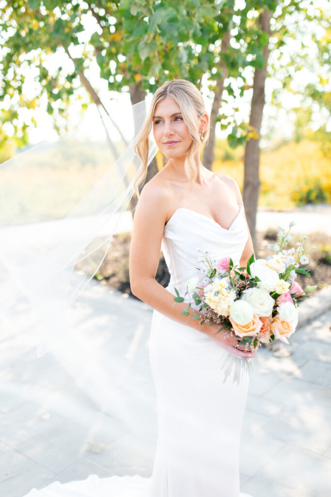 A bride holding her bouquet looking off while her veil flows.
