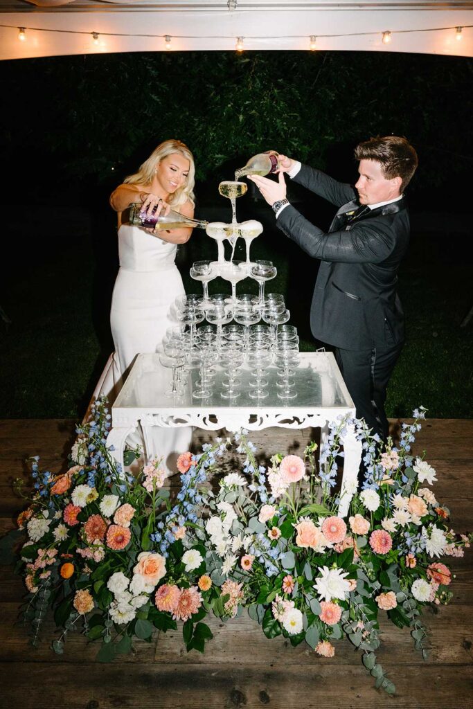 A couple pouring champagne from a tower of glasses