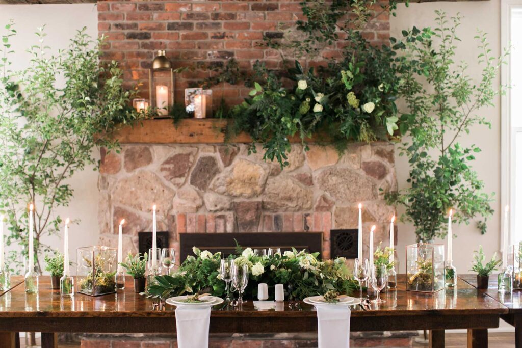 A tablescape with flowers and candles with a fireplace behind.