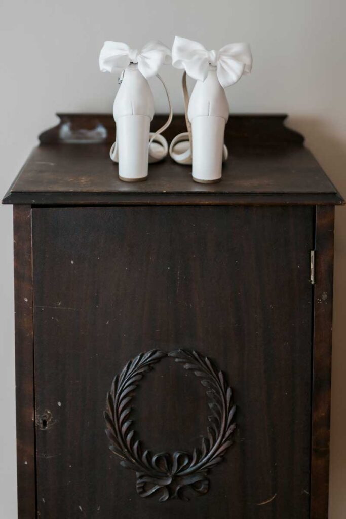 white high heels with bows on the back on top of a wooden table