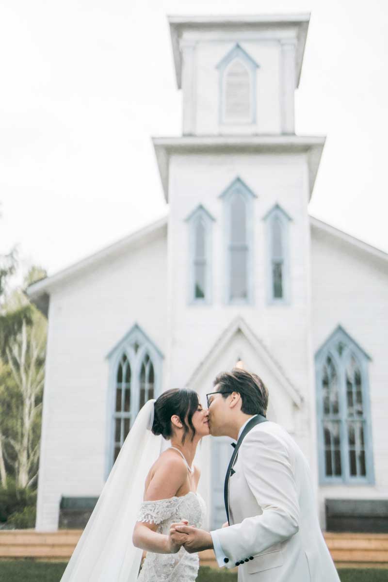 bride and groom kiss in front of cranberry creek chapel