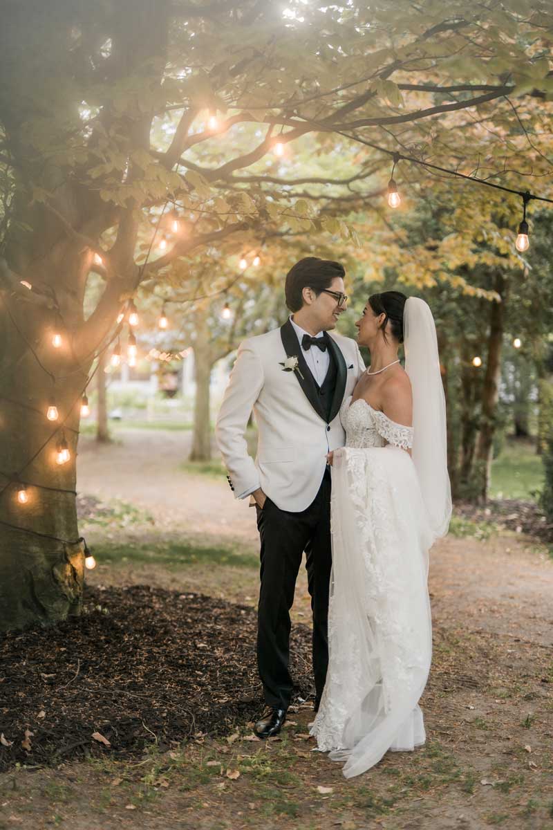 bride and groom standing under tree decorated with twinkle lights
