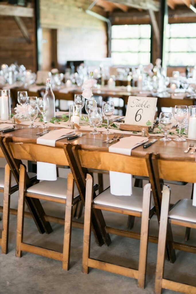 harvest tables with wooden chairs set for a wedding reception