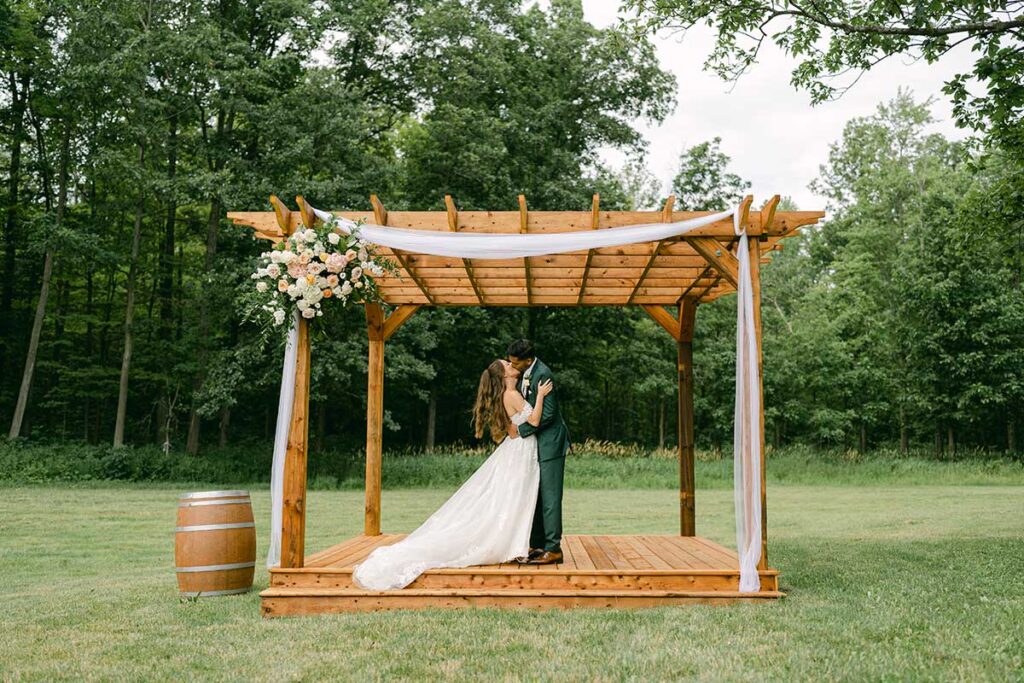 bride and groom under wooden ceremony arbour